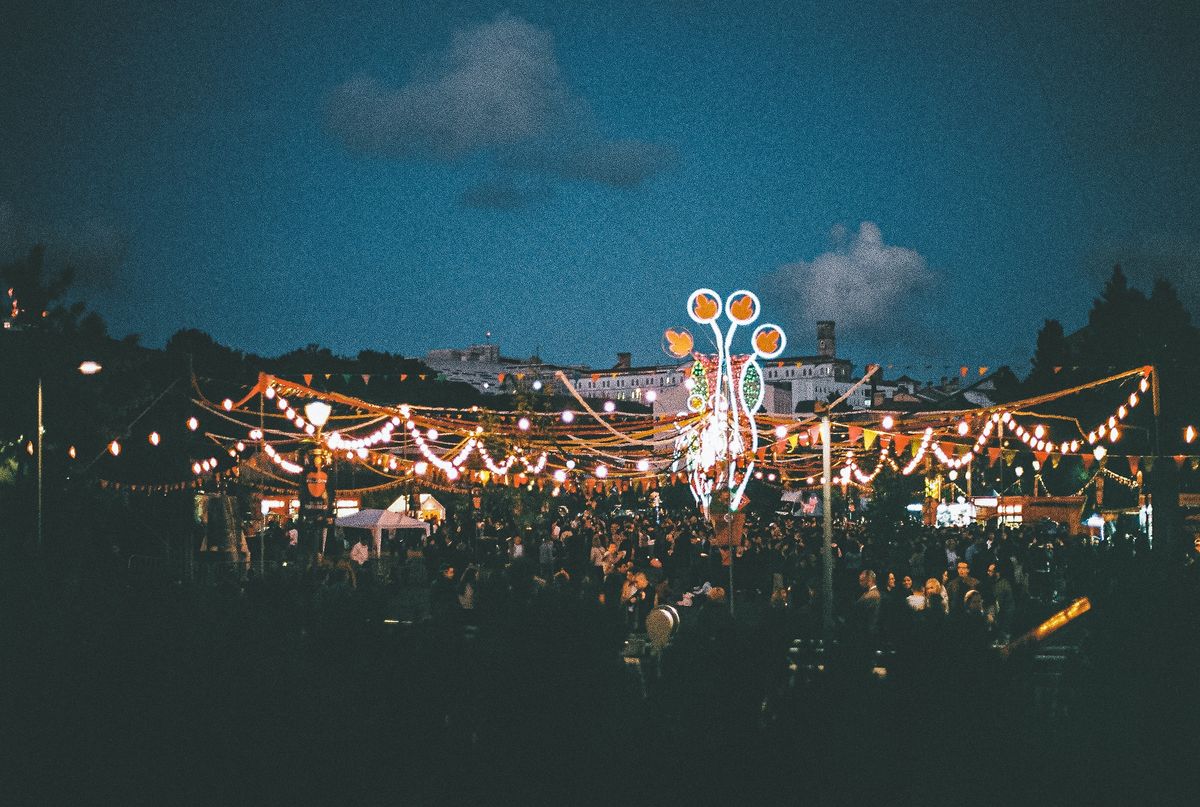 A crowd of people gather at tables under lights and banners and a dark-blue sky